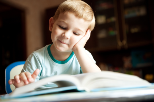 young boy smiling as he reads a book