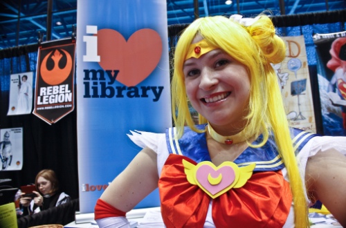 Woman in Sailor Moon costume stands in front of i heart my library banner