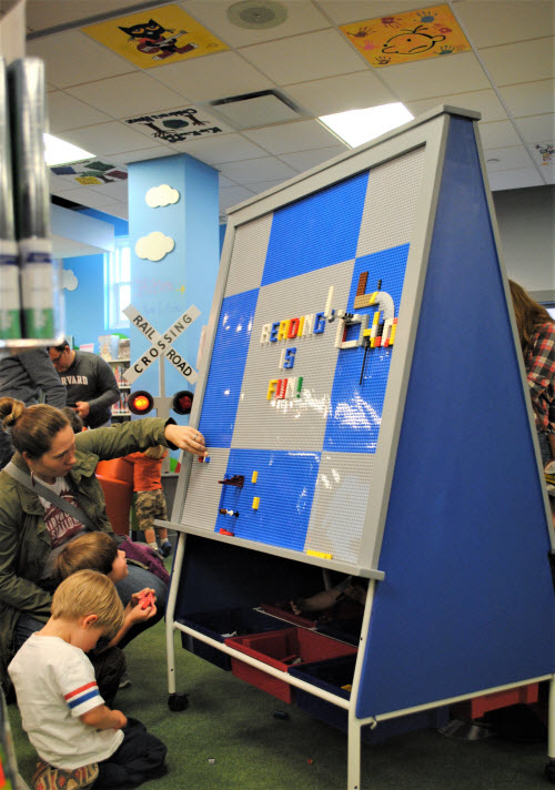 Photo of a large LEGO easel and on the ceiling are tiles painted by library patrons.
