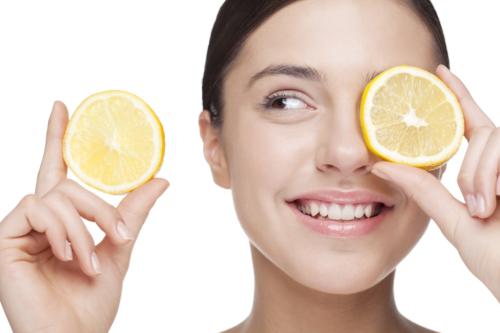 Smiling woman holding lemon slice over one eye