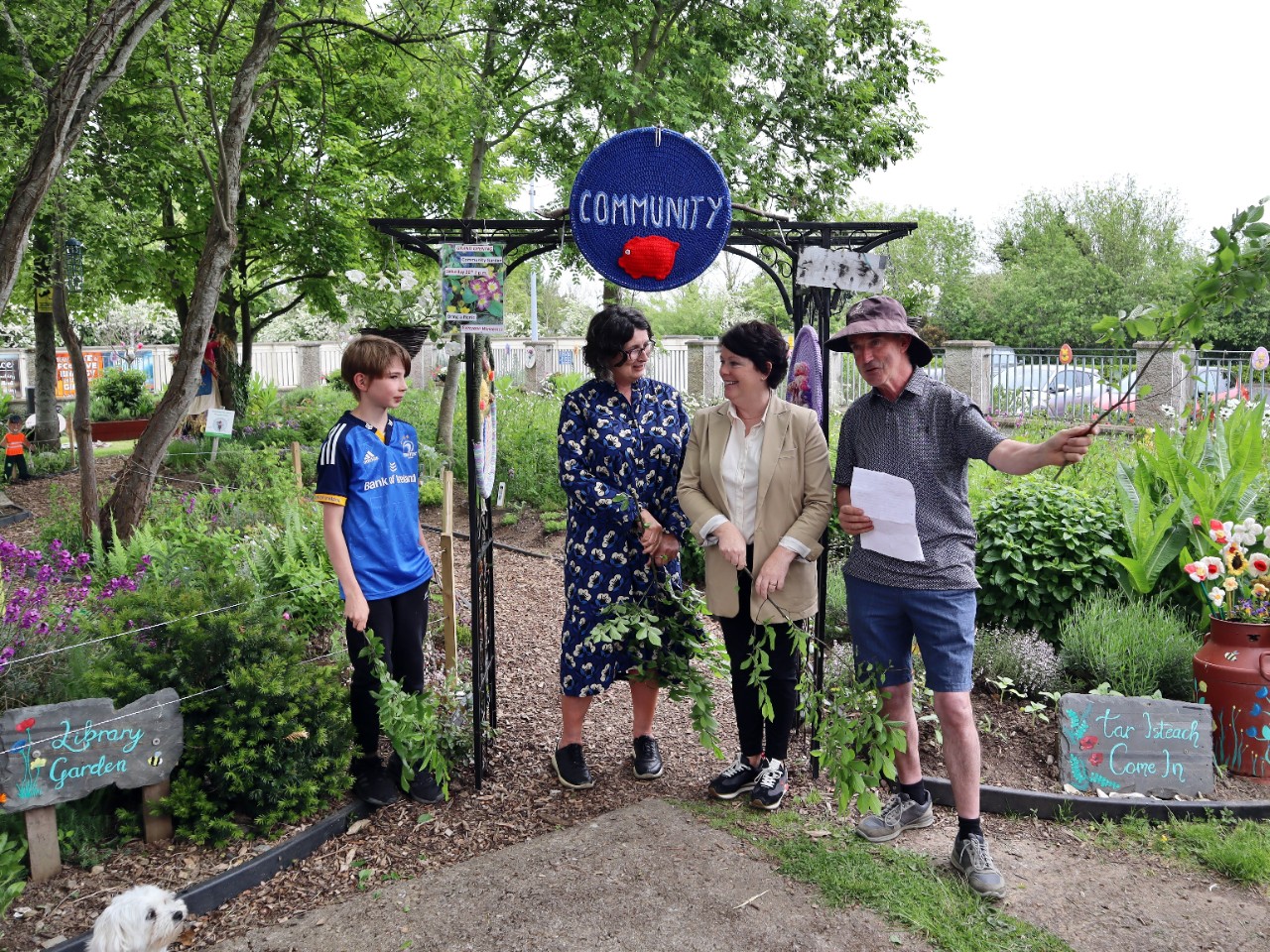 Group of people standing in a garden, in front of an arched sign that reads ‘Community’