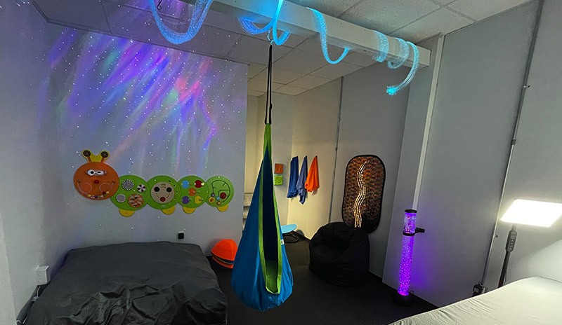 sensory room with a swing chair, SAD lamp, crash pad, and other sensory items