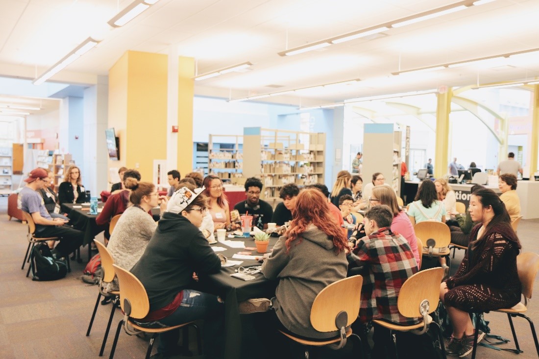 group of people seated around a table with bookshelves in the background