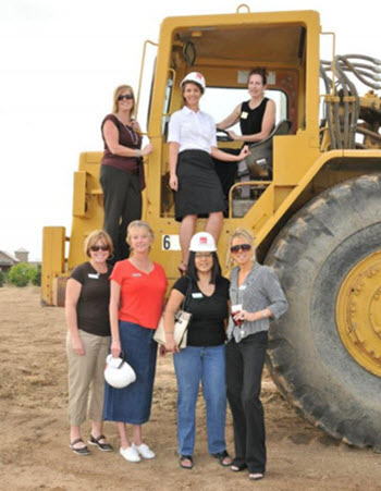 A group of people pose in front of construction equipment.