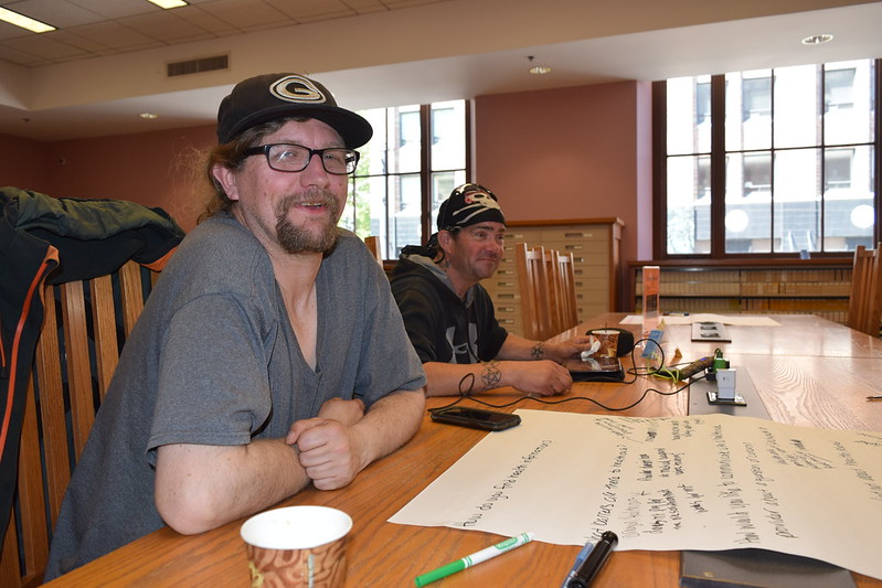 two men seated at a table with paper and markers two men seated at a table with paper and markers