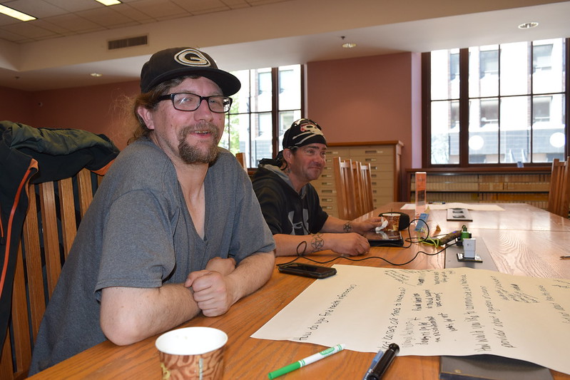 two men seated at a table with paper and markers 