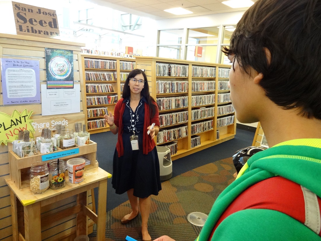 Woman giving a demonstration to a visitor in front of a seed library display