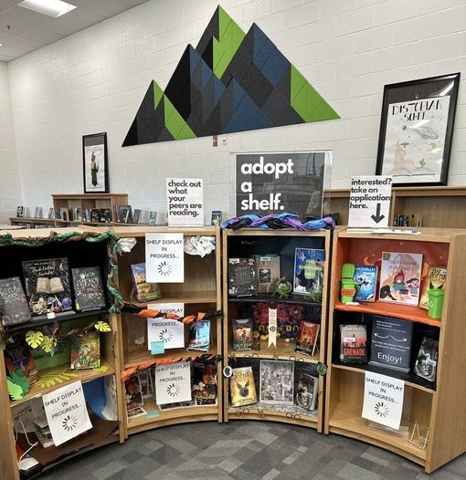 Four bookshelves with custom displays and sign that reads: adopt a shelf