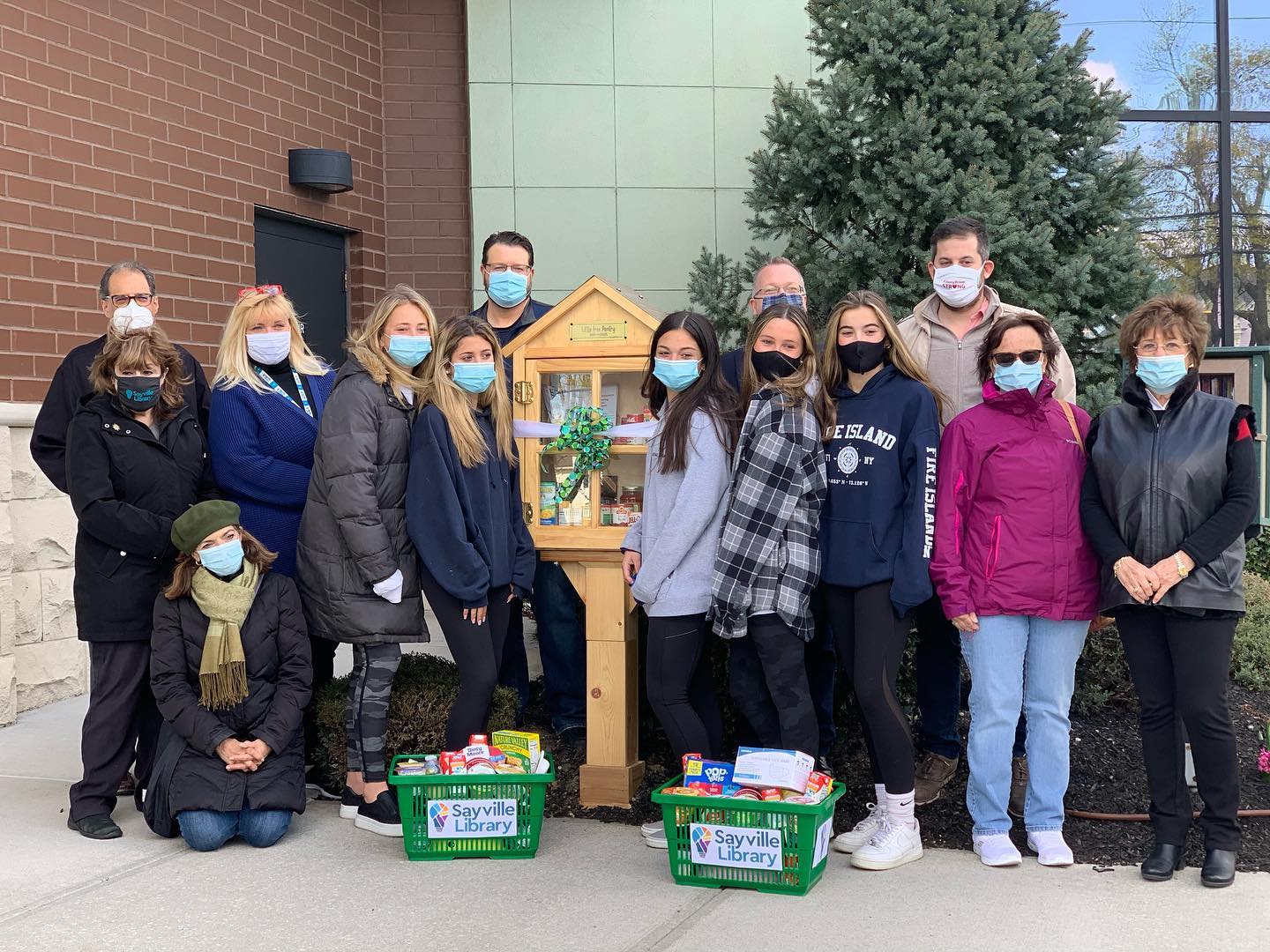 Group of people standing next to a new little free library, with a bow on the outside 