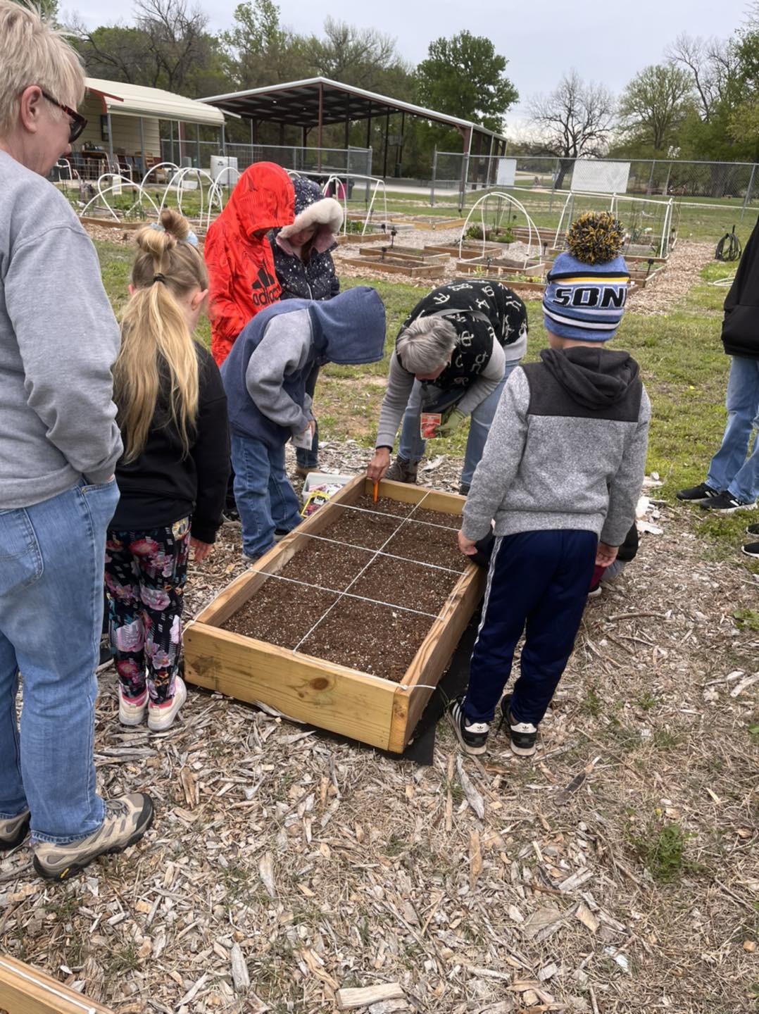 Group of children and two adults planting a square foot garden