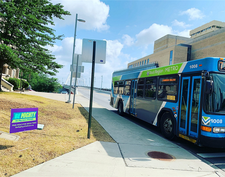 City bus on the street near a sign that reads ‘Be Mighty’ 