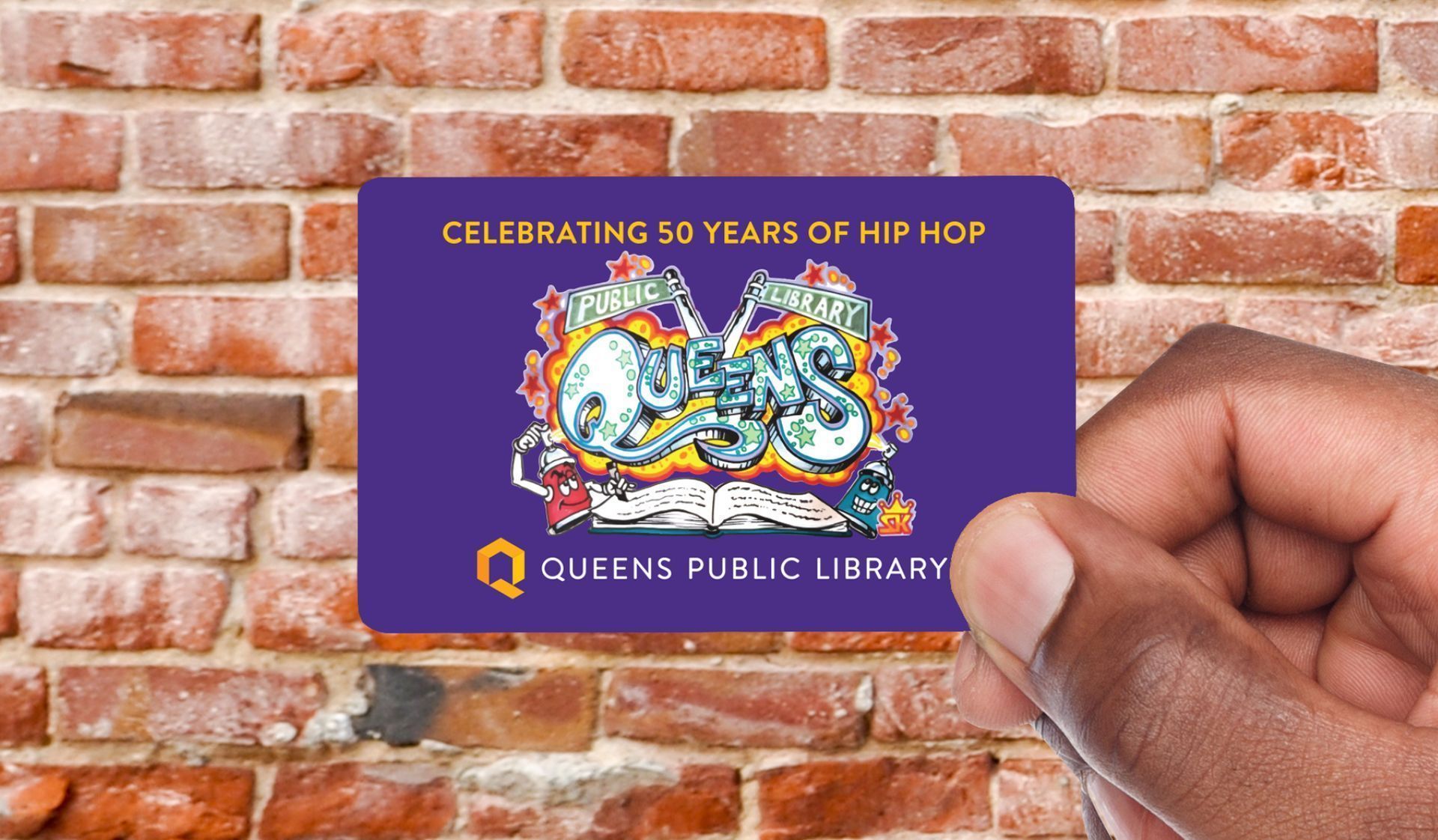 Queens Public Library special edition card, Hand holding a copy of the Queens Public Library special edition card, with an image of graffiti art and the words ‘celebrating 50 years of Hip Hop’