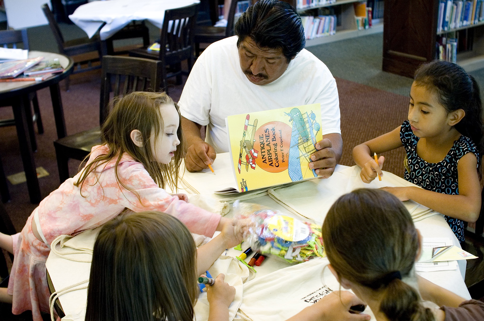Man and a group of children seated together at a library table doing an art activity