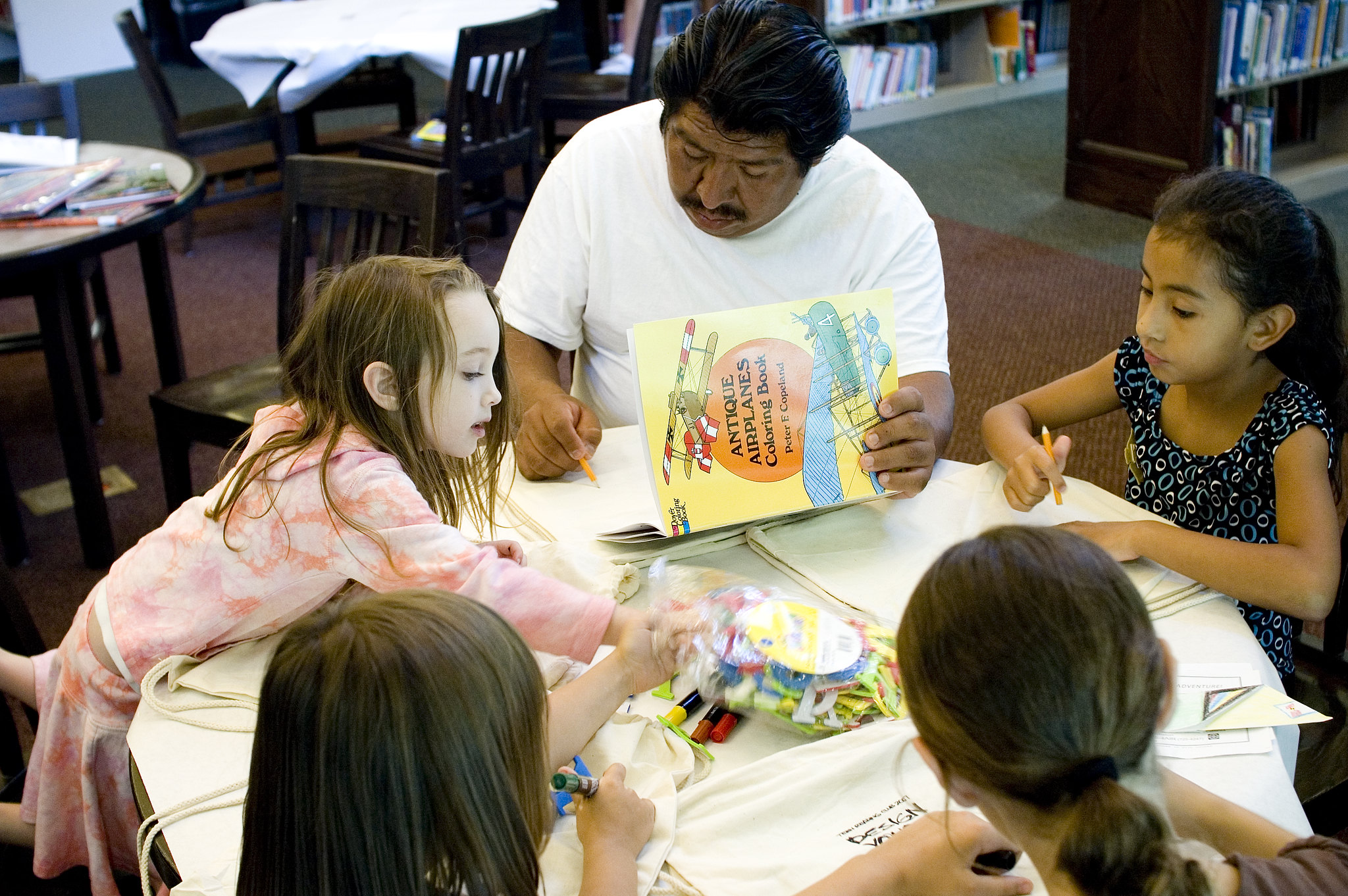 Man and a group of children seated together at a library table doing an art activity Man and a group of children seated together at a library table doing an art activity