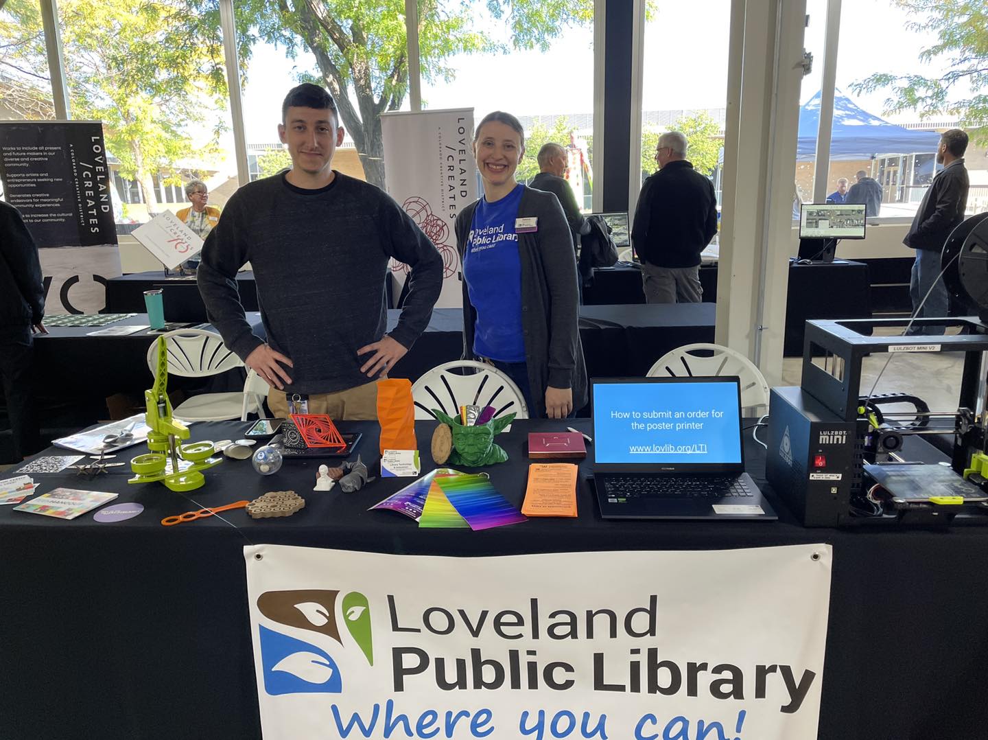 Loveland Innovation Celebration Two smiling library staff members standing at a table with a sign that reads ‘Loveland Public Library where you can’