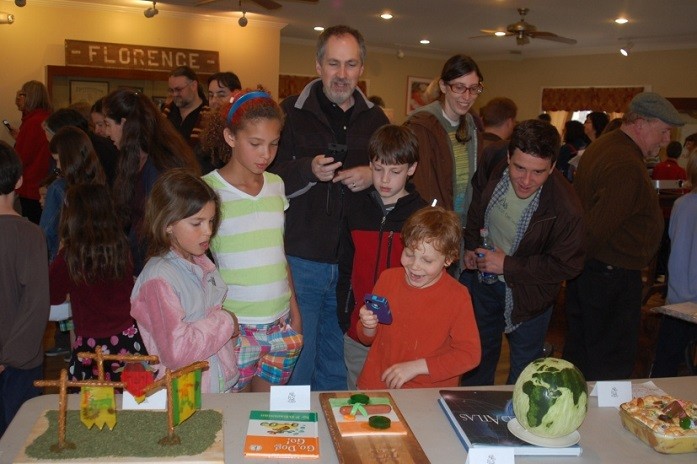 A man and several smiling children viewing edible books displayed on a table