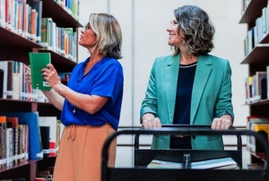 Courtesy of Kansas City Public Library Two individuals organizing books on shelves in a library setting, with a book cart in the foreground.