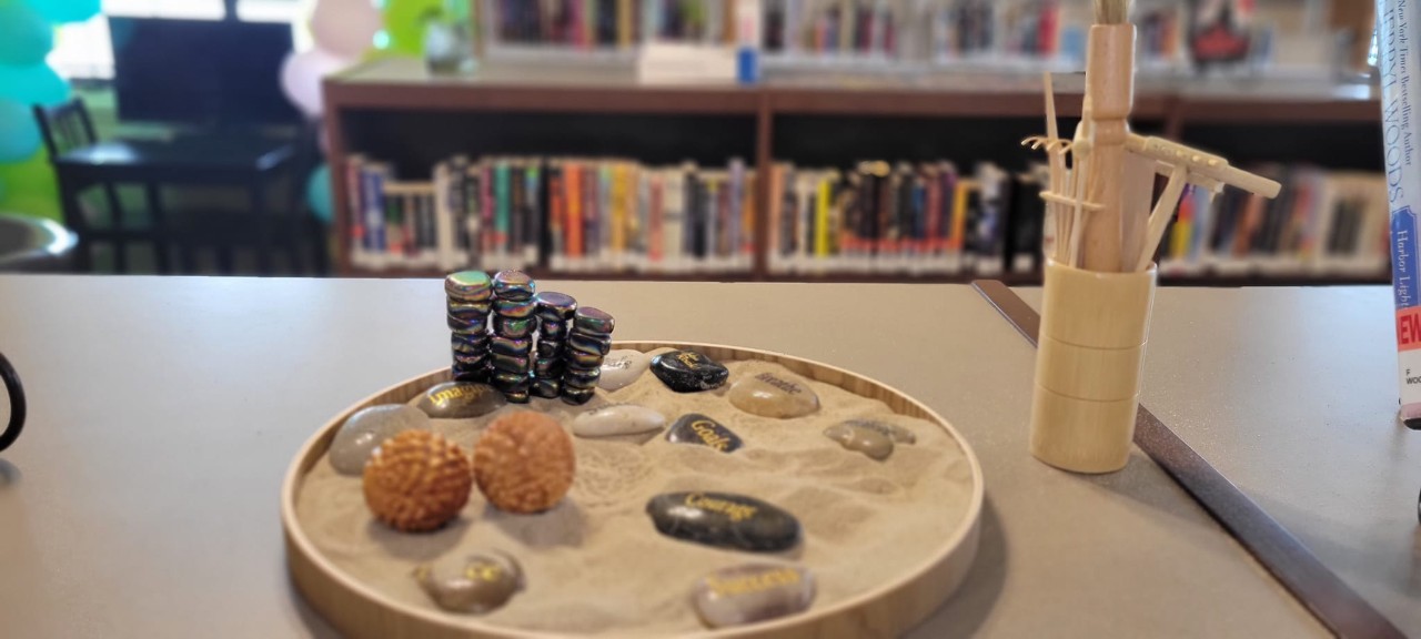 close-up image of a Zen sand garden on a table with bookshelves in the background