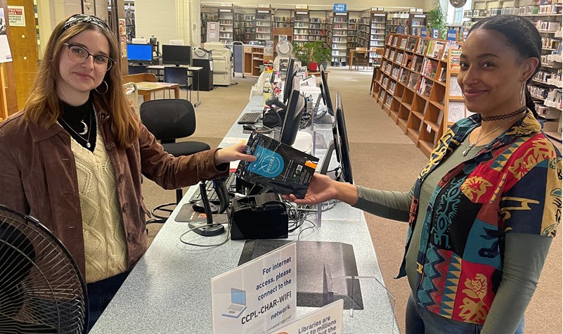 Two smiling young women standing at a library desk with Deterra drug disposal pouches