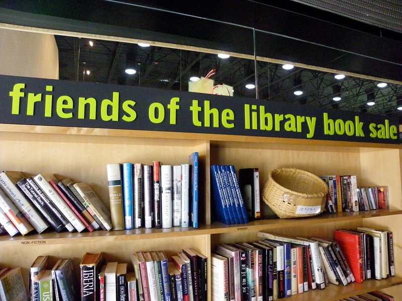 Close-up of two bookshelves with a sign above the shelves reading ‘friends of the library book sale’